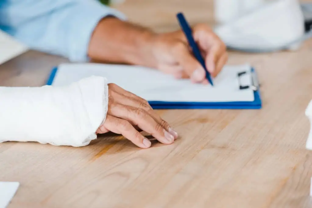 A person wearing a cast is filling out paperwork with a personal injury attorney. 