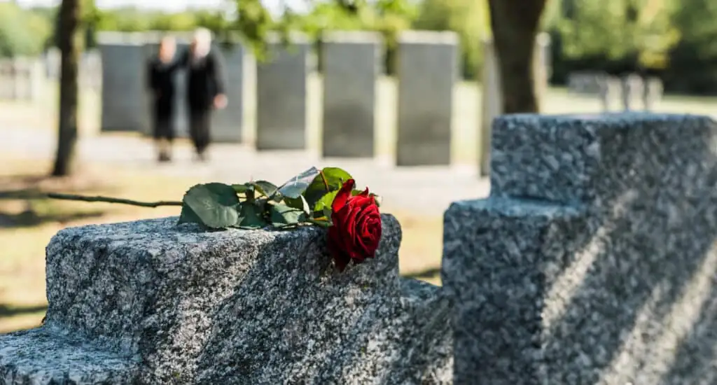 Rose on gravestone, mourners in background. Houston wrongful death attorney.